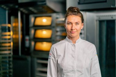 Fırının arka planında profesyonel üniformalı gülümseyen bir aşçı kadın fırının portresi ve taze pişmiş yiyecekler.