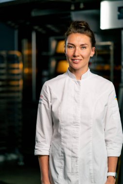 Fırının arka planında profesyonel üniformalı gülümseyen bir aşçı kadın fırının portresi ve taze pişmiş yiyecekler.