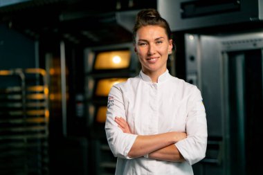 Fırının arka planında profesyonel üniformalı gülümseyen bir aşçı kadın fırının portresi ve taze pişmiş yiyecekler.