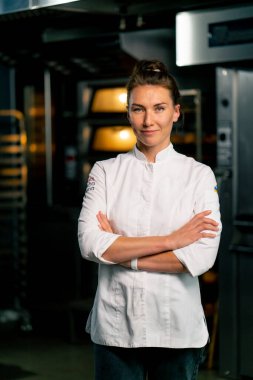 Fırının arka planında profesyonel üniformalı gülümseyen bir aşçı kadın fırının portresi ve taze pişmiş yiyecekler.