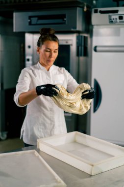 Profesyonel kadın fırıncı sıcak bir fırında taze ekmek pişirmek için hamuru dikkatle yoğurur.