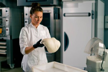 Profesyonel kadın fırıncı sıcak bir fırında taze ekmek pişirmek için hamuru dikkatle yoğurur.