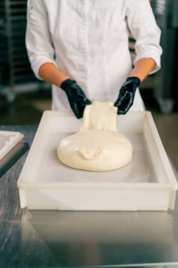 Eldivenli kadın ellerinin yakın plan çekimi taze hamur işleri pişirmek için hamur işini ekmek tepsisine koyuyor.