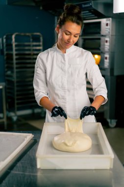 Profesyonel kadın fırıncı sıcak bir fırında taze ekmek pişirmek için hamuru dikkatle yoğurur.