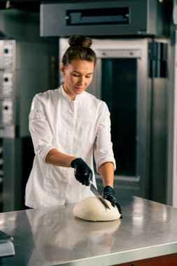 Mutfaktaki profesyonel kadın fırıncı ekmek ve baget pişirmek için dondurulmuş hamur kesiyor.