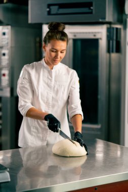 Mutfaktaki profesyonel kadın fırıncı ekmek ve baget pişirmek için dondurulmuş hamur kesiyor.