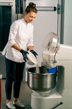 Kadın fırıncı lezzetli ekmek hazırlamak için mutfak gezegen mikserine hamur koyuyor.