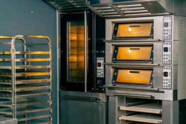 Profesyonel bir fırın mutfağında büyük miktarda fırın malzemesi pişirmek için önceden ısıtılmış sıcak fırını çalıştırdım.