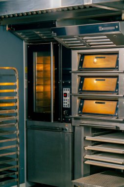 Profesyonel bir fırın mutfağında büyük miktarda fırın malzemesi pişirmek için önceden ısıtılmış sıcak fırını çalıştırdım.
