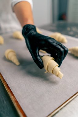 Kadın bir fırıncının ellerinin yakın plan çekimleri pişmemiş kruvasanları fırında pişirmek için parşömen ile birlikte pişirme tepsisine yerleştirirken.