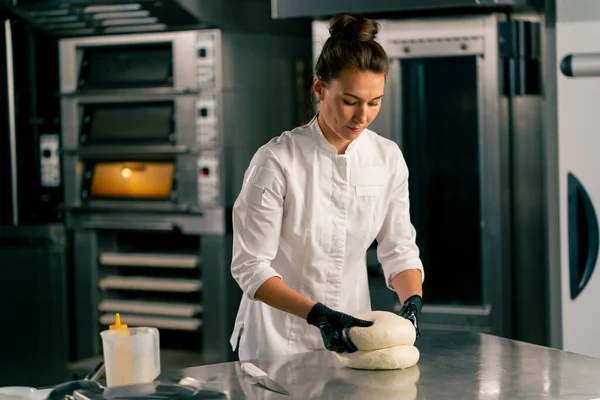 プロフェッショナル女性パン屋は 居心地の良いベーカリーで新鮮なパンを焼くための生地を慎重に練ります — ストック写真