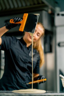 Pasta şefi bir hamur işi dükkanında tatlı hazırlamak için eritilmiş beyaz çikolatayla metal bir spatulayı karıştırıyor.