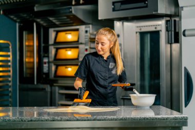 Bir kız şekerci, şekerci dükkanında şeker ve tatlı yapmak için metal spatula kullanarak çikolataya sinirleniyor.