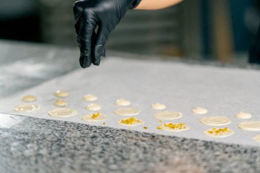 Bir şekerlemecinin eldivenli eli üzerine doğal çikolata şekerlemeleri ve doğranmış fındıklar serper.