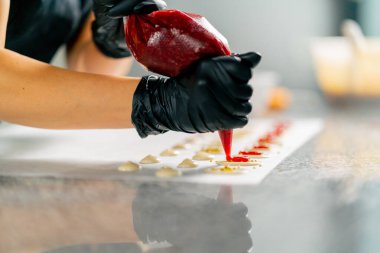 Bir hamur işi şefinin eldivenli eli, meyveli çikolataları pasta poşetinden çıkarır.