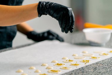 Bir şekerlemecinin eldivenli eli üzerine doğal çikolata şekerlemeleri ve doğranmış fındıklar serper.