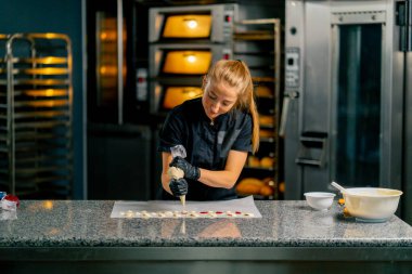 Bir pastacı, pastanedeki bir pastanenin parşömenine doğal şeker şeklinde çikolata sıkıyor.