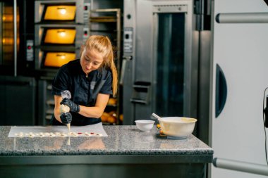 Bir pastacı, pastanedeki bir pastanenin parşömenine doğal şeker şeklinde çikolata sıkıyor.