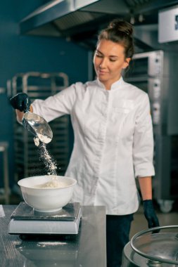 Kadın fırıncı taze pişmiş yiyecekler hazırlamak için hamur yoğurmak için karıştırıcıya buğday unu döker.