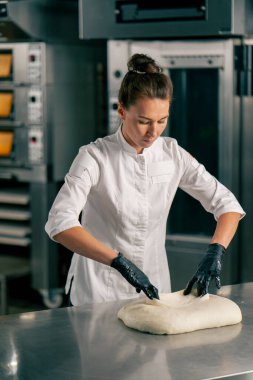 Üniformalı kadın fırıncı fırında pişirmeden önce hamuru mutfak yüzeyinde kruvasan şekline sokuyor.