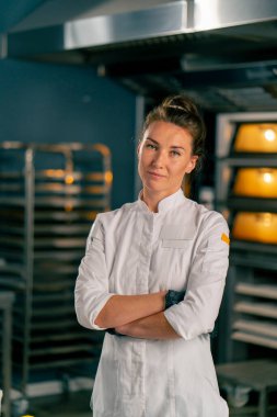 Kadın bir fırıncı, fırının arka planında profesyonel bir mutfak yüzeyinin arkasında duruyor ve kameraya bakıyor.