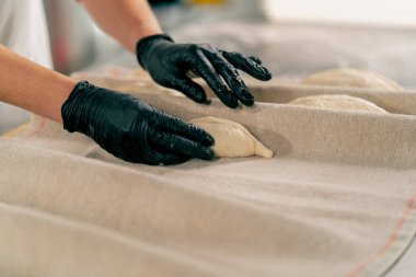 Bir fırında ekmek hazırlamak ve pişirmek için hamuru dikkatle yoğuran bir kadın şefin yakın çekimi.