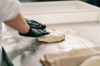 Bir fırında ekmek hazırlamak ve pişirmek için hamuru dikkatle yoğuran bir kadın şefin yakın çekimi.