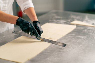 Bir fırında ekmek hazırlamak ve pişirmek için hamuru dikkatle yoğuran bir kadın şefin yakın çekimi.