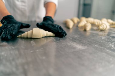 Şefin eldivenli ellerine yakın çekim. Hamuru şekillendirip bükerek kruvasan şekline sokuyor.