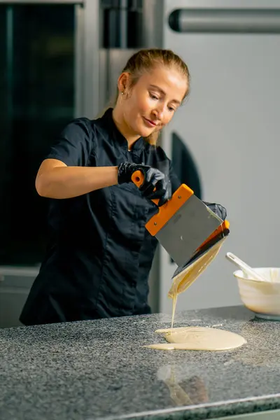 A girl confectioner tempers chocolate using a metal spatula for making sweets and desserts in a confectionery shop