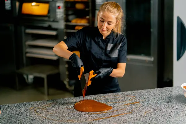 A confectioner tempers chocolate before preparing desserts using a metal spatula on a kitchen surface