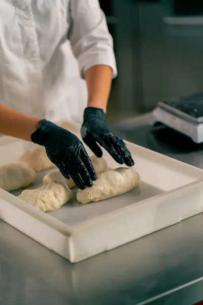 在厨房的表面上 一个穿着均匀滚动面团的女面包师的戴着手套的手的特写镜头变成了羊角面包形状 — 图库照片