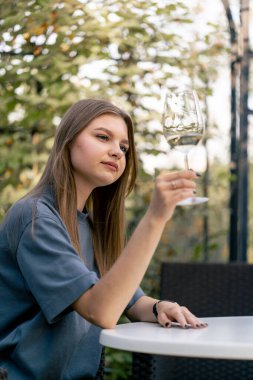 Düşünceli bir kız bahçedeki güzel bir kemerde oturur bir bardak şarapla dikkatlice tadına bakar.