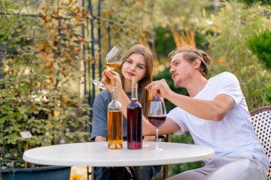 A couple of a guy and a girl are sitting together at a table in the garden of a winery and tasting different types of wine clipart