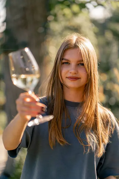 美しい長髪の少女の肖像画は グラスからワインを一杯飲んで笑顔でカメラに手渡す — ストック写真