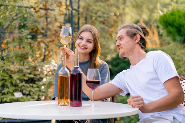 Bir çift adam ve bir kız şaraphanenin bahçesinde bir masada birlikte oturuyorlar ve farklı türde şarap içiyorlar.