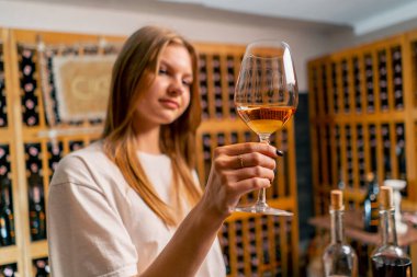 Güzel bir kız elinde bir bardak şarap tutuyor ve şarap mahzenindeki tatma sırasında kalitesini kontrol ediyor.