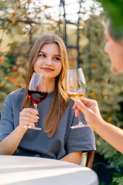 Close-up shot of a girl clinking glasses with different types of wine with a guy sitting together on the terrace