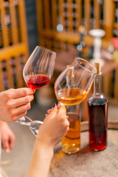 Close-up shot of a man and woman\'s hands holding glasses of different types of wine and clinking glasses at a tasting in the cellar
