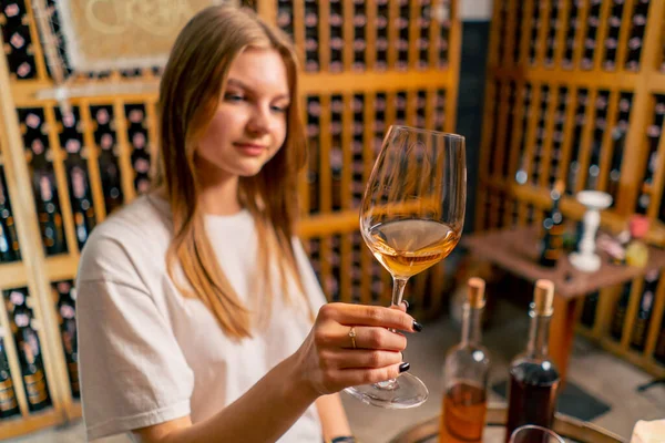 Güzel bir kız elinde bir bardak şarap tutuyor ve şarap mahzenindeki tatma sırasında kalitesini kontrol ediyor.