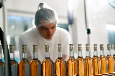 A male technologist controls the process of packaging and distribution of wine bottles in production clipart