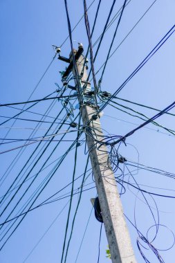 Güçlendirilmiş beton bir yüksek voltaj direğinde, bir direkte birçok kablo bulunan kaotik olarak birbirine bağlı elektrik ve optik kablolar.