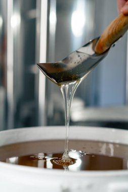 Yakından çekilen metal kaşık doğal sıvı balı karıştırıyor ve büyük bir kaseye geri akıyor.