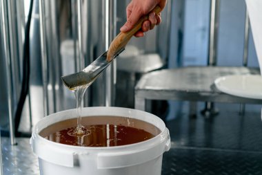 Yakından çekilen metal kaşık doğal sıvı balı karıştırıyor ve büyük bir kaseye geri akıyor.