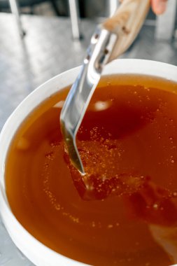 Özel bir metal kaşığın üst çekimi, doğal sıvı balı karıştırır ve büyük bir kaseye geri akar.