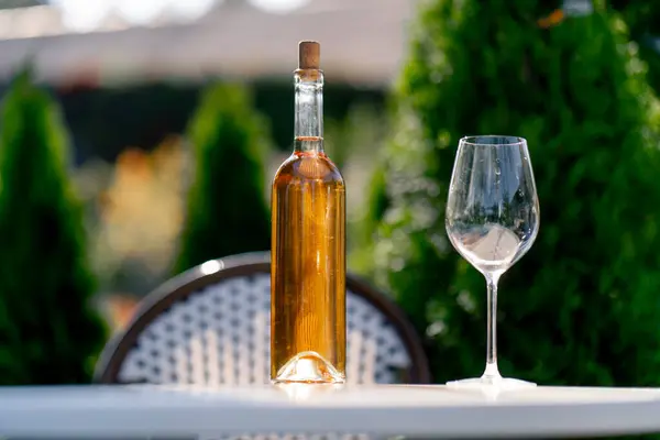 Close-up shot of a glass bottle with wine and a glass stand on the table of a summer terrace of a restaurant for tasting