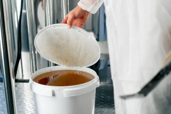 The hand of a technologist opens a barrel of natural liquid honey to be added to the production of drinks
