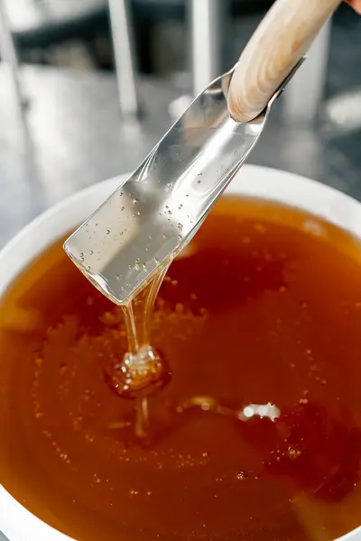 Top shot of a special metal spoon mixing natural liquid honey which flows back into a large bowl