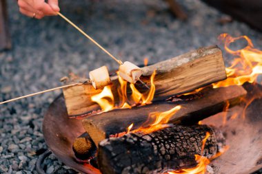 Gün batımında birkaç kişinin odun ateşinde marşmelov kızartırken yakın plan çekimleri.
