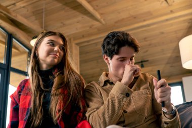 Genç aşıklar kanepede otururken TV kumandası için gülüp kavga ediyorlar.